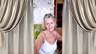 A cheerful housewife twerks in the kitchen near the washing machine and beckons with her bare feet.